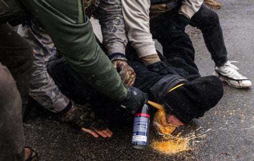 Federal agents fire pepper spray at a protester pinned to the ground.