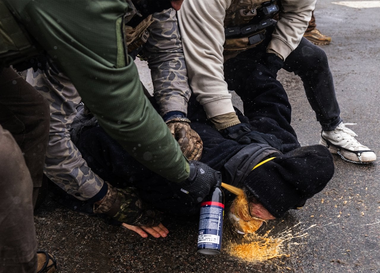 Federal agents fire pepper spray at a protester pinned to the ground.